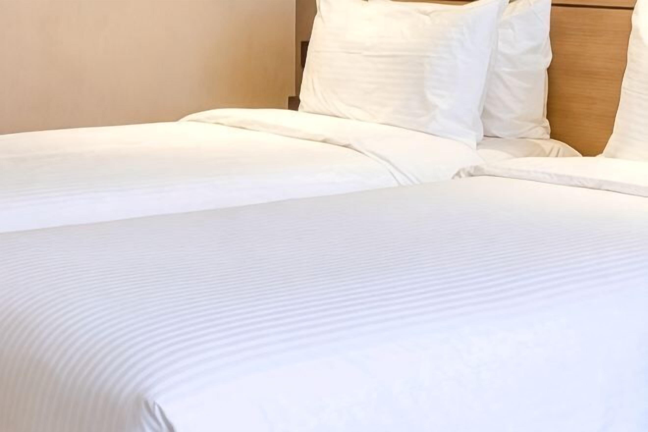 A neatly made bed with white linens and pillows.
