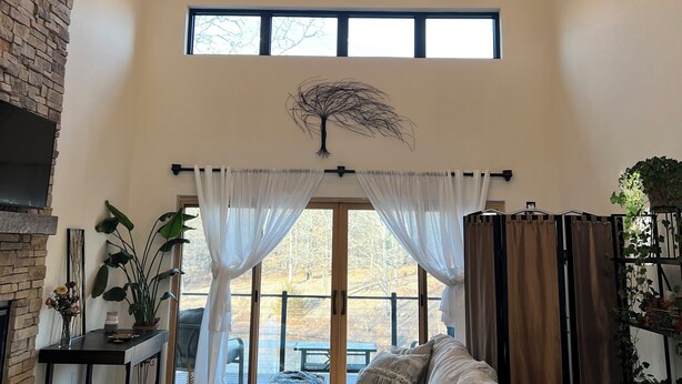 A spacious living room with a high ceiling, a chandelier, a fireplace, and a large window with curtains. - Beautiful Modern mountain getaway overlooking water with fountain. (Joplin)