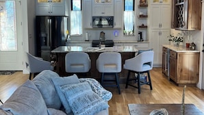 A modern kitchen with a central island, white cabinetry, and a dining area with bar stools. - Beautiful Modern mountain getaway overlooking water with fountain. (Joplin)