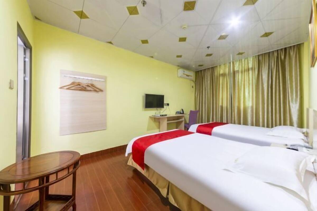 A hotel room with two beds, a desk, a chair, a TV, and a coat rack.