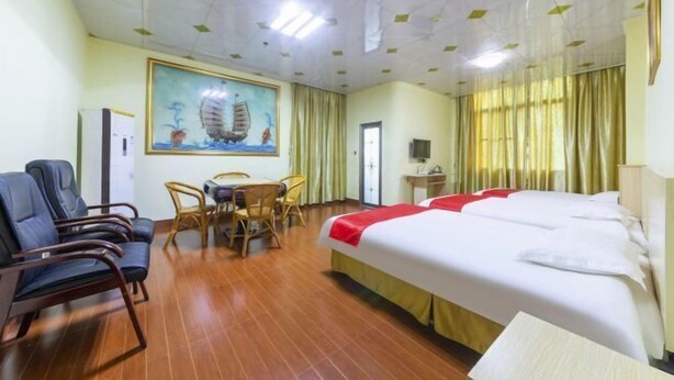 A hotel room with a bed, a desk, a chair, a table, and a painting on the wall. - He Long Hotel (Shaoguan)