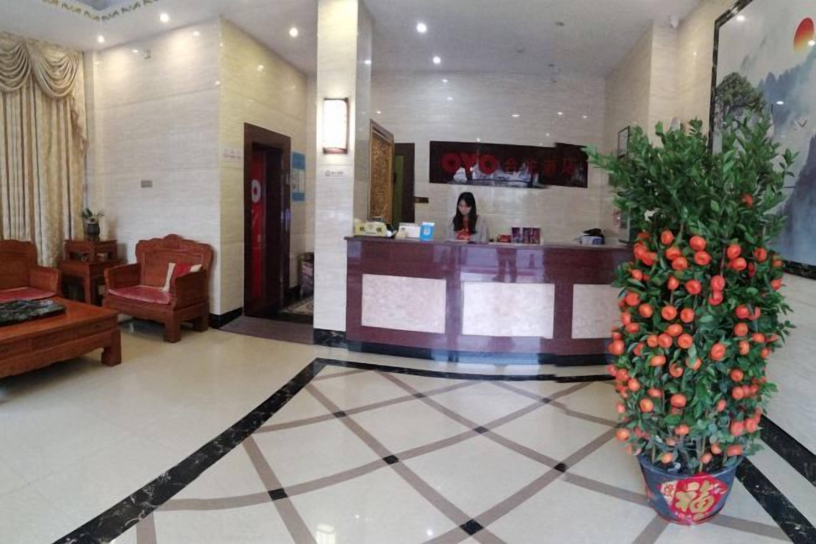 A hotel lobby with a reception desk, seating area, and a large potted plant.