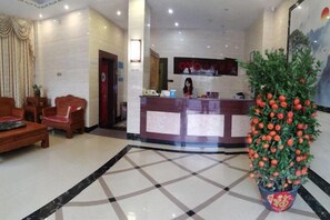 A hotel lobby with a reception desk, seating area, and a large potted plant. - He Long Hotel (Shaoguan)