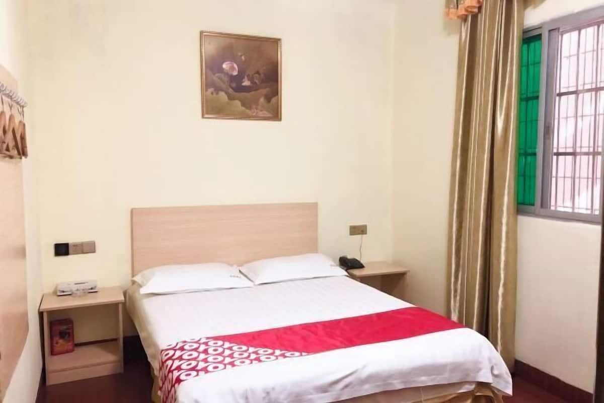 A hotel room with a bed, a nightstand, a painting on the wall, and a window with curtains.