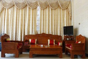 A traditional living room with a sofa set, coffee table, and armchairs, a television, and curtains. - He Long Hotel (Shaoguan)