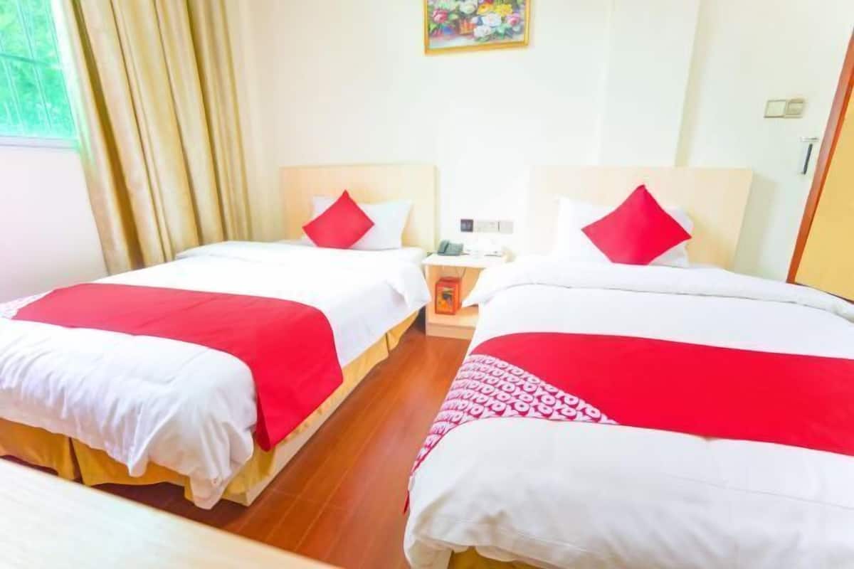 A hotel room with two beds, each with white and red bedding, a wooden floor, a nightstand with a phone, and a painting on the wall.