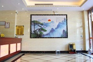A hotel lobby with a reception desk, a large wall painting of a mountain landscape, and a tiled floor. - He Long Hotel (Shaoguan)