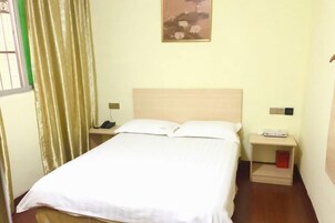A neatly made bed with white linens, a wooden headboard, a bedside table with a lamp, and a nightstand with a phone.