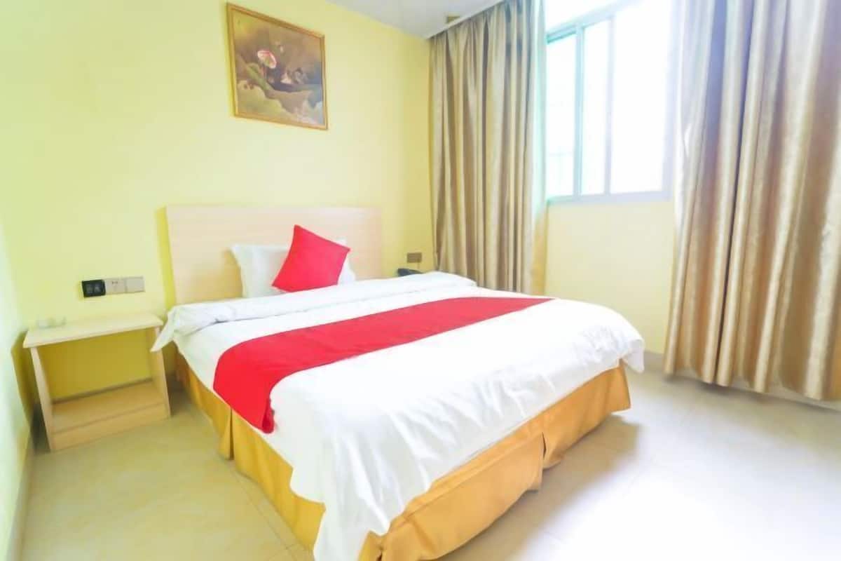 A hotel room with a bed, a nightstand, a painting on the wall, and a window with curtains.