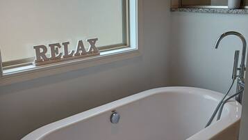 A modern bathroom with a freestanding bathtub, a window with frosted glass, and a mirror above the sink.