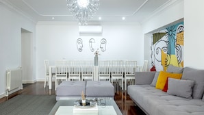 Een moderne woonkamer met een glazen salontafel, een grijze bank en een eetgedeelte met witte stoelen.