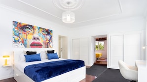 Een moderne slaapkamer met een groot bed, een heldere plafondlamp en een kleurrijk abstract schilderij erboven.
