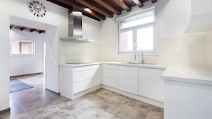 Een moderne keuken met witte kasten, een roestvrijstalen afzuigkap, een raam met zonwering en een klok aan de muur.