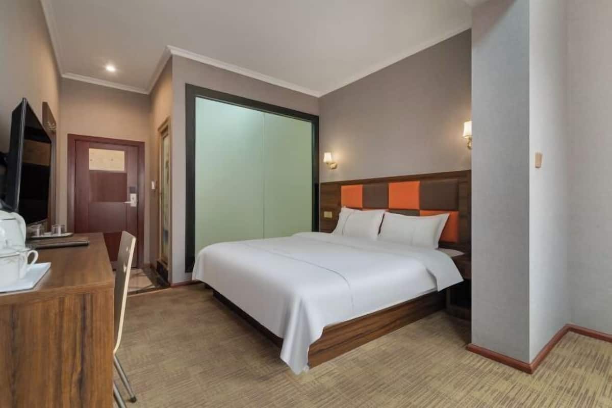 Ein Hotelzimmer mit einem Bett, einem Schreibtisch mit Stuhl, einem Fernseher und einer Tür.
