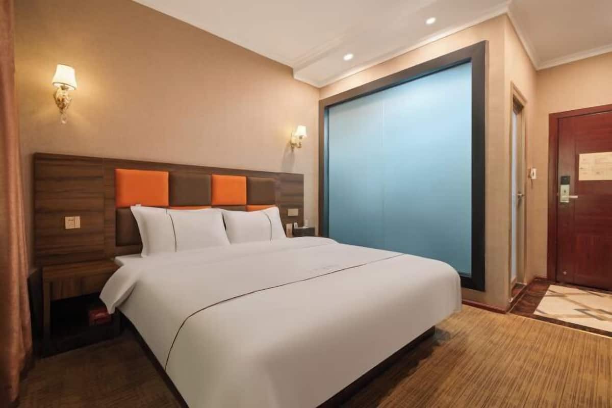 Ein Hotelzimmer mit einem großen Bett, einem hölzernen Kopfteil, zwei Wandleuchten, einer blauen Schiebetür und einer Holztür.