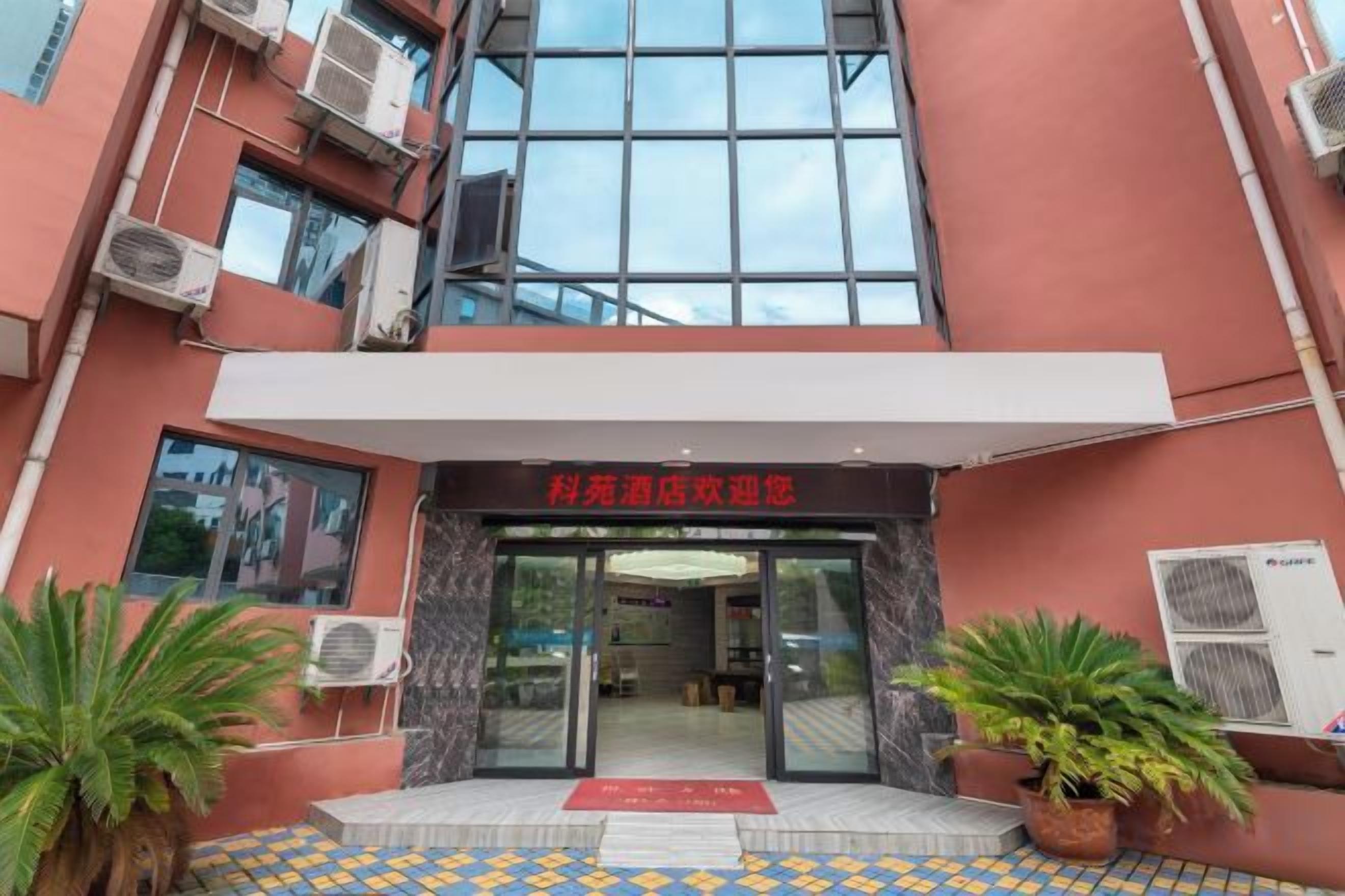 Entrada de un edificio con toldo rojo, unidades de aire acondicionado y plantas en macetas.