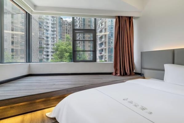 A hotel room with a large window, a bed, and a view of high-rise buildings.