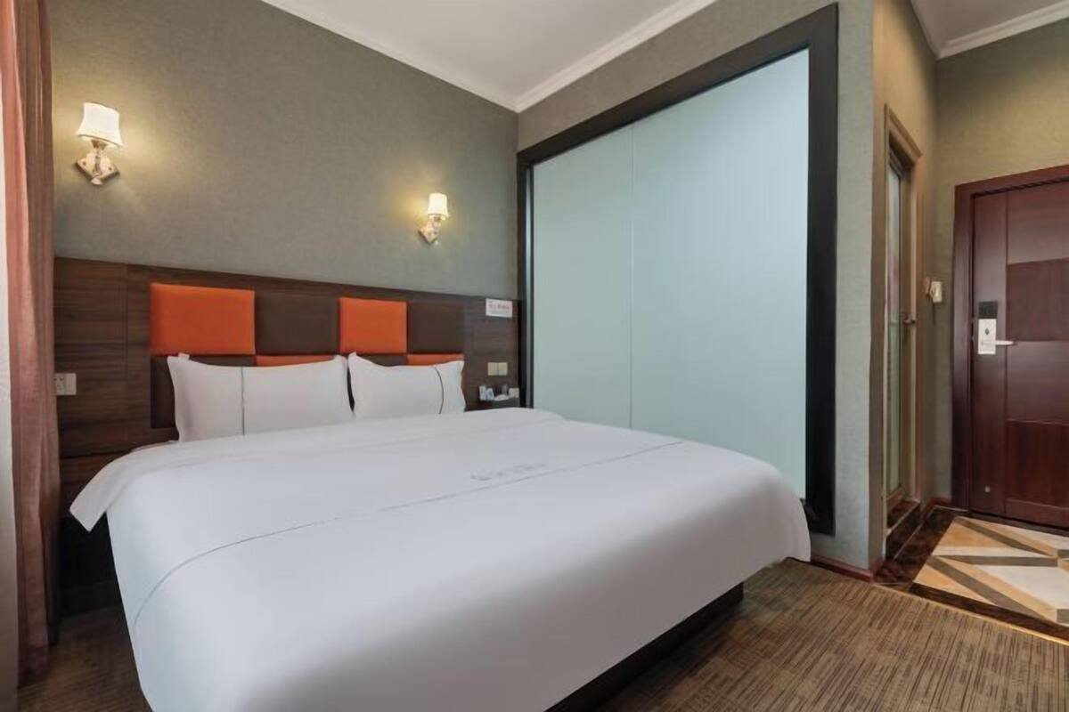 Ein Hotelzimmer mit einem großen Bett, zwei Wandlampen, einem Holz-Kopfteil und einer Schiebetür.