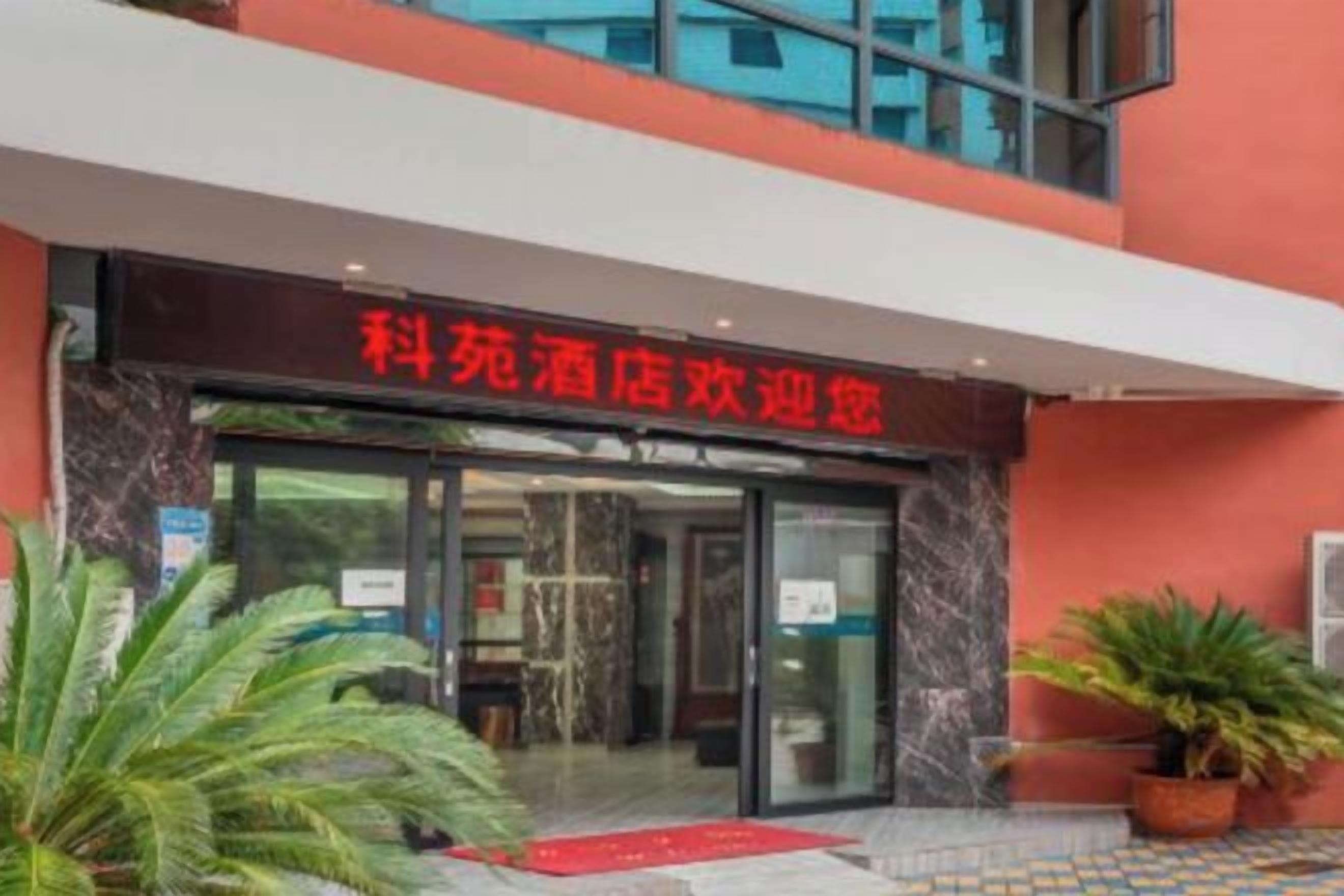 A hotel entrance with a red sign, glass doors, and potted plants.