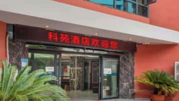 A hotel entrance with a red sign, glass doors, and potted plants.