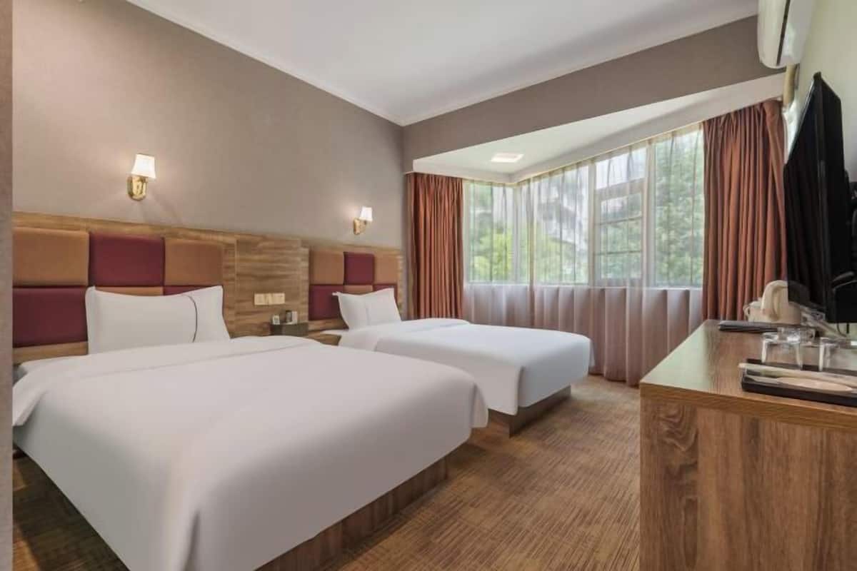 Ein Hotelzimmer mit zwei Betten, einem Holzkopfende, einem Schreibtisch mit Stuhl und einem Fenster mit Vorhängen.