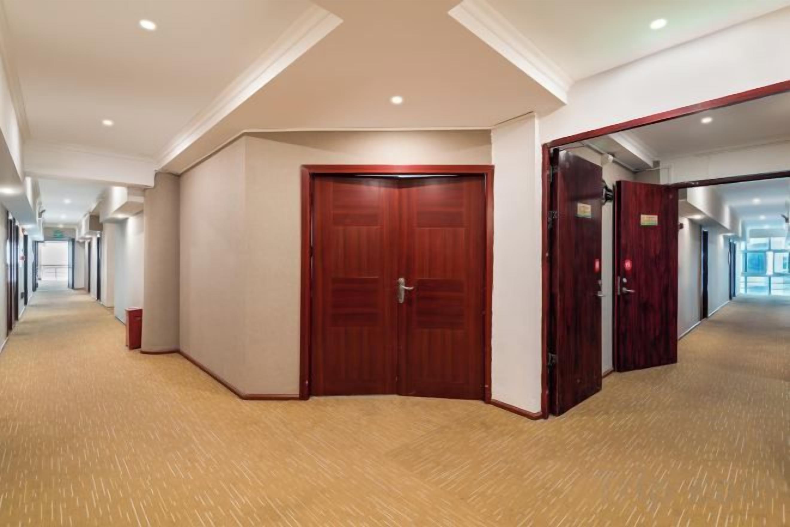 A hotel corridor with wooden doors, carpeted floors, and a ceiling with recessed lighting.