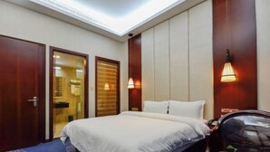 A hotel room with a bed, a desk, a chair, a small table with a plant, and a wall-mounted lamp. - The Tophams Hotel Suez (Wenzhou)