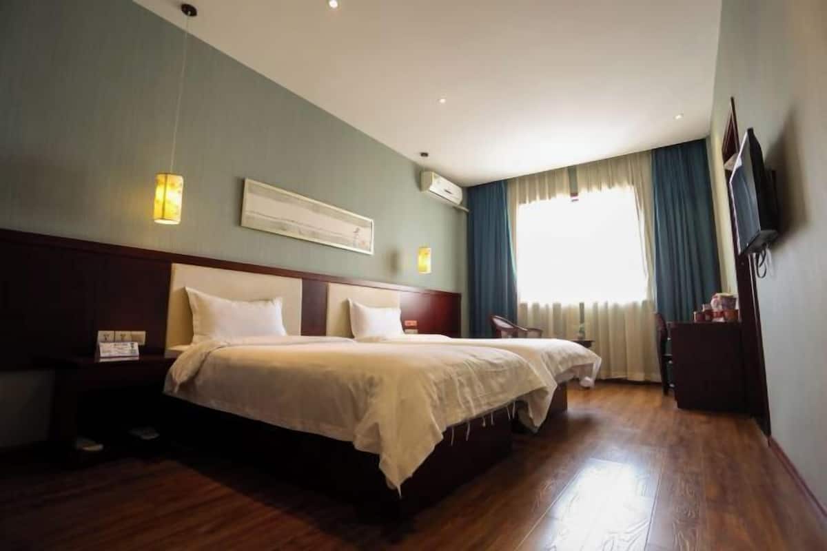 A hotel room with a large bed, a bedside table, a TV, and a window with curtains.