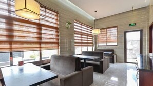 A modern hotel lobby with a seating area, large windows with blinds, and a reception desk. - The Tophams Hotel Suez (Wenzhou)