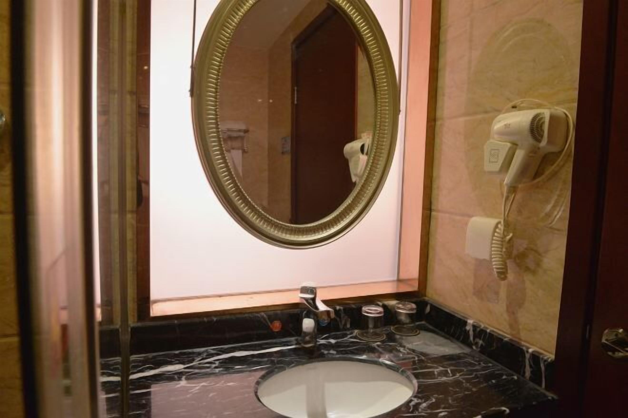 A bathroom with a marble sink, a round mirror, and a hairdryer mounted on the wall.