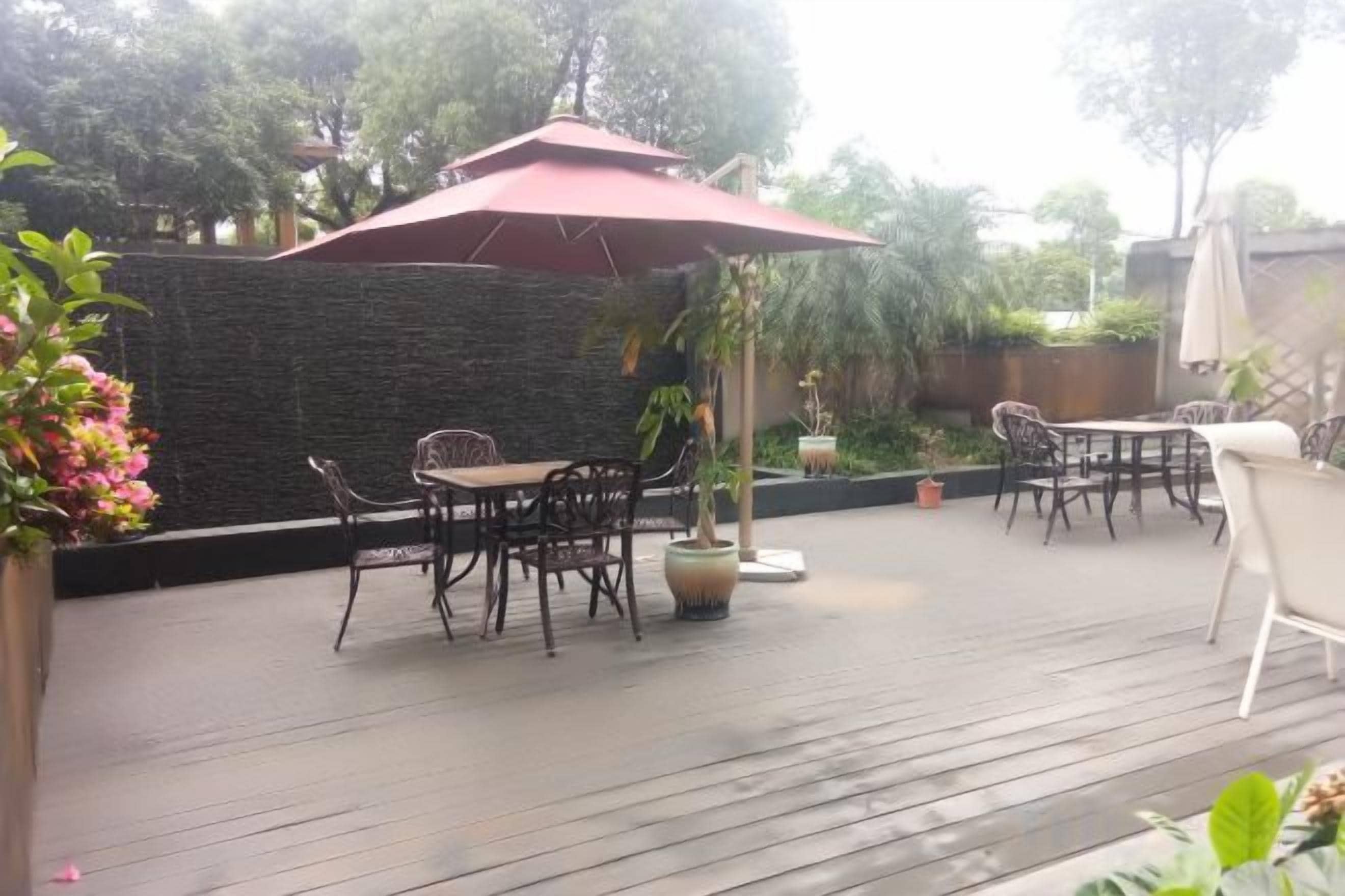 Une terrasse extérieure avec une table et des chaises, un parasol rouge et des plantes en pot.