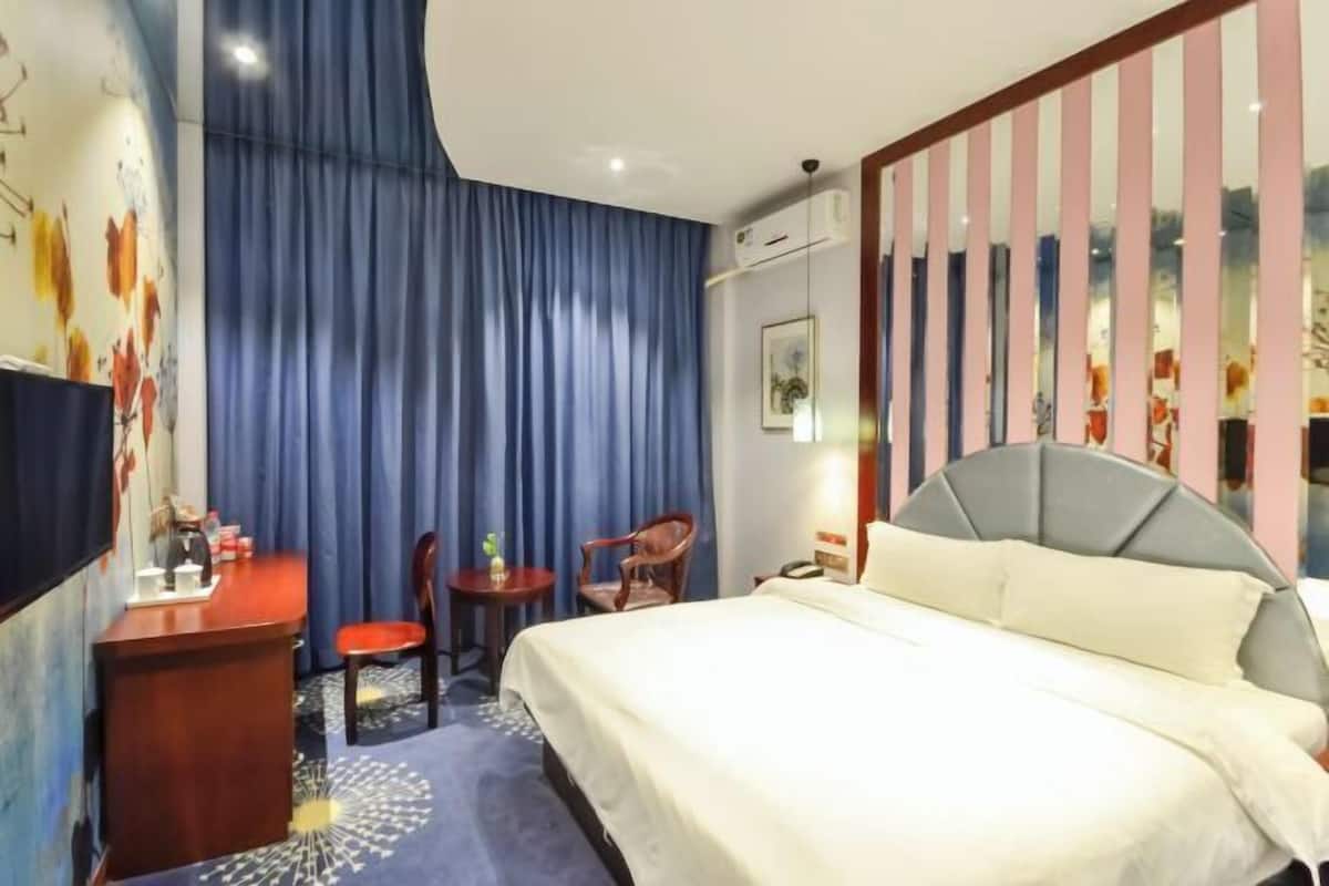 A hotel room with a bed, a desk, a chair, and a blue curtain.