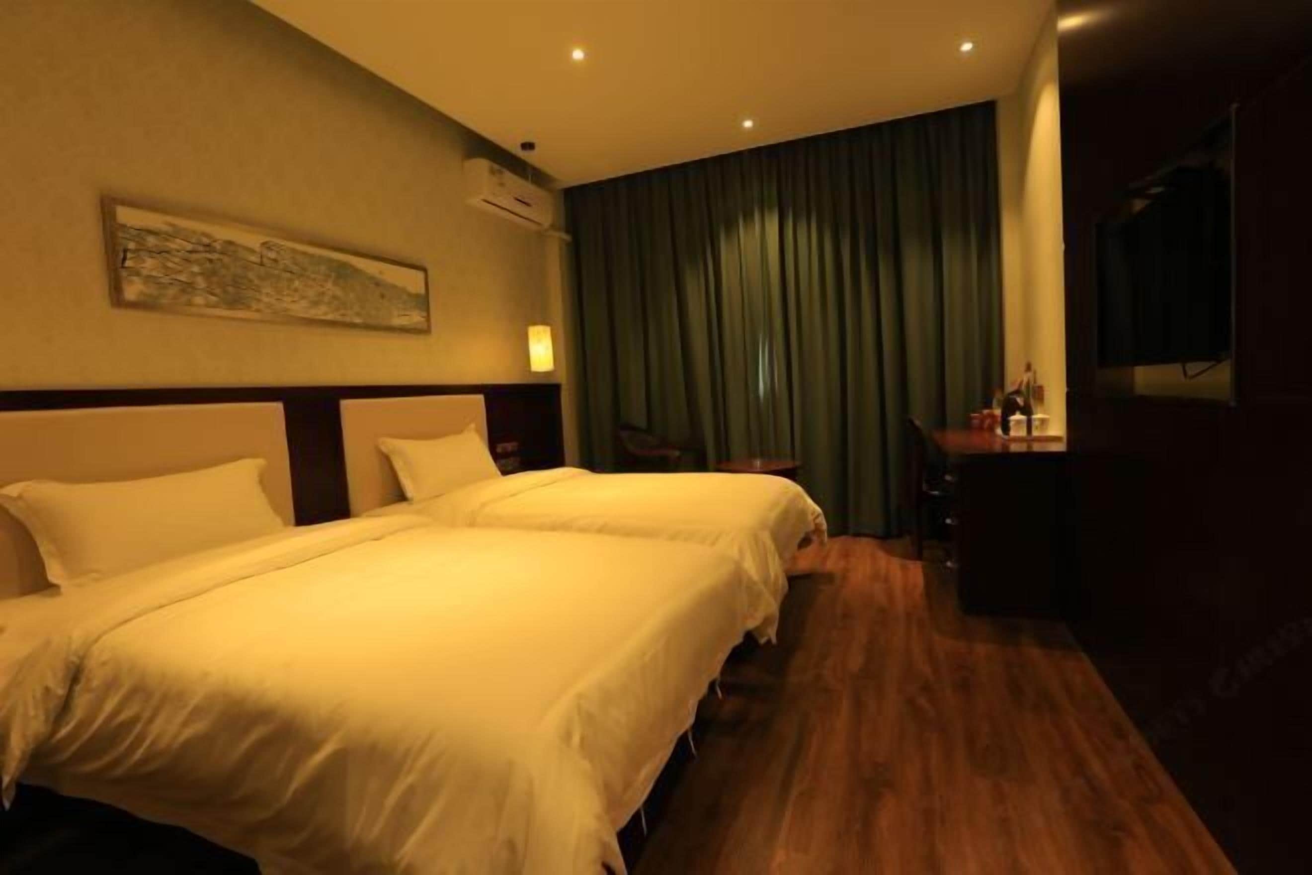 Quarto de hotel com duas camas, uma escrivaninha, uma cadeira, uma televisão e um quadro na parede.