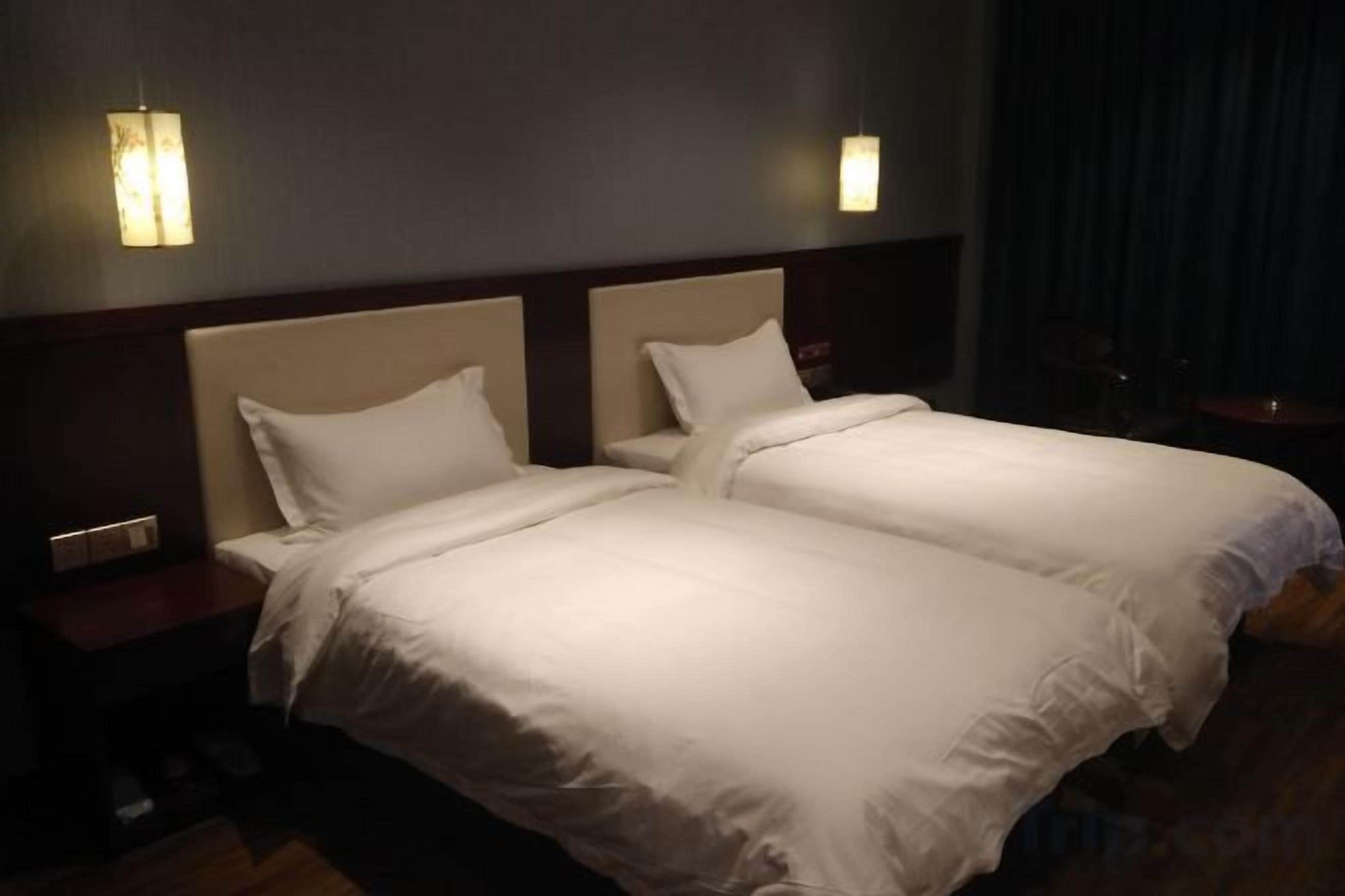 A hotel room with two beds, a nightstand, and wall-mounted lamps.