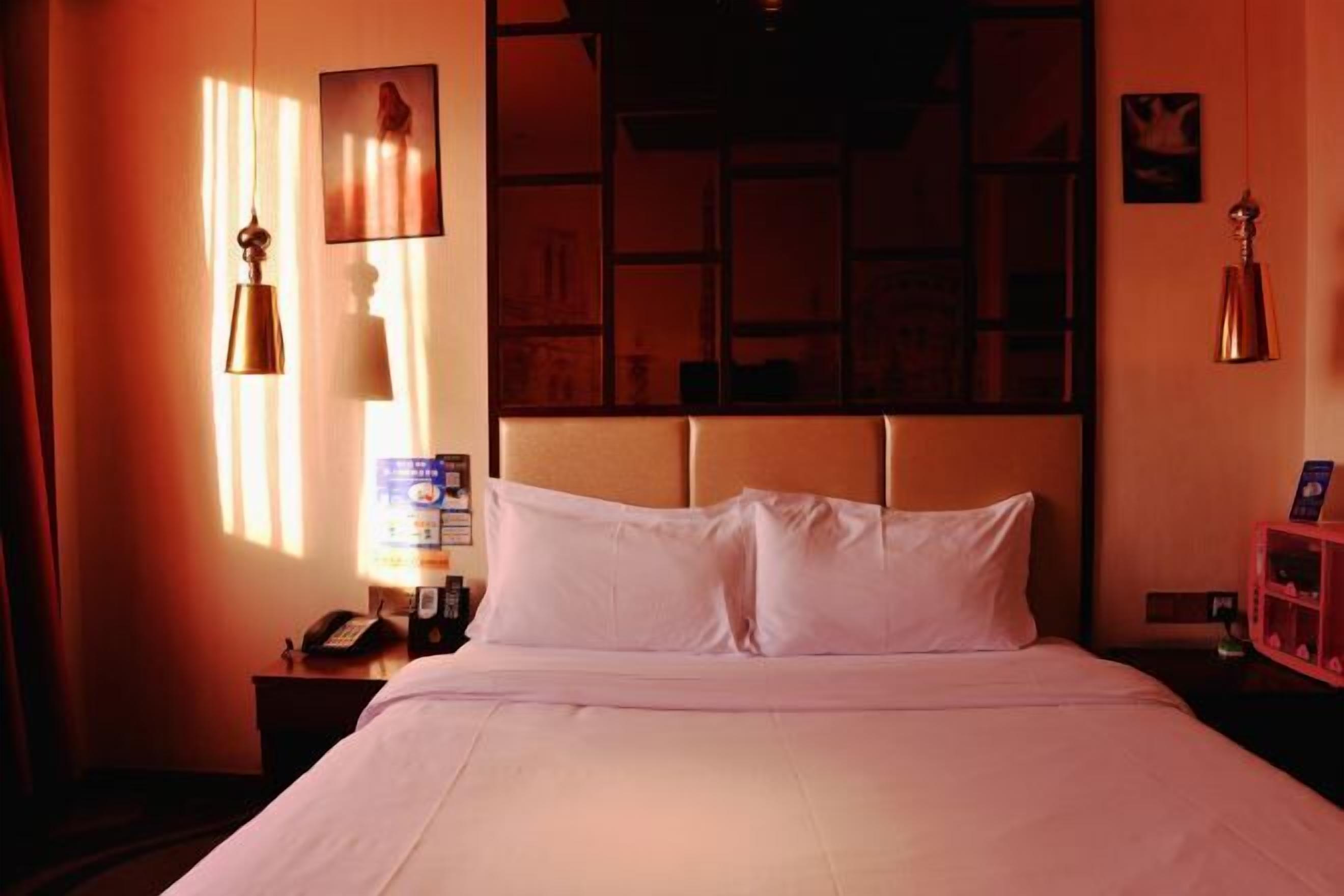 A hotel room with a bed, a nightstand, a telephone, and a wall-mounted shelf with a book.