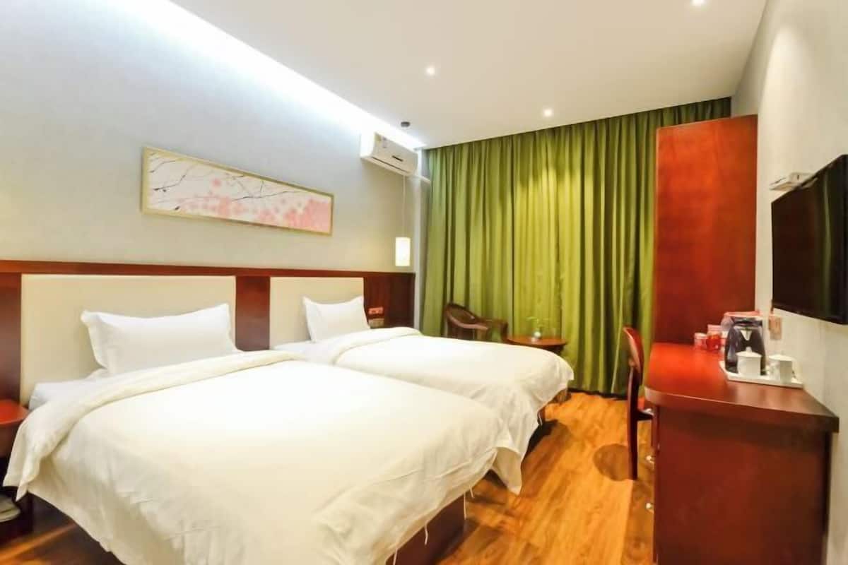 A hotel room with two beds, a desk, a chair, and a television.