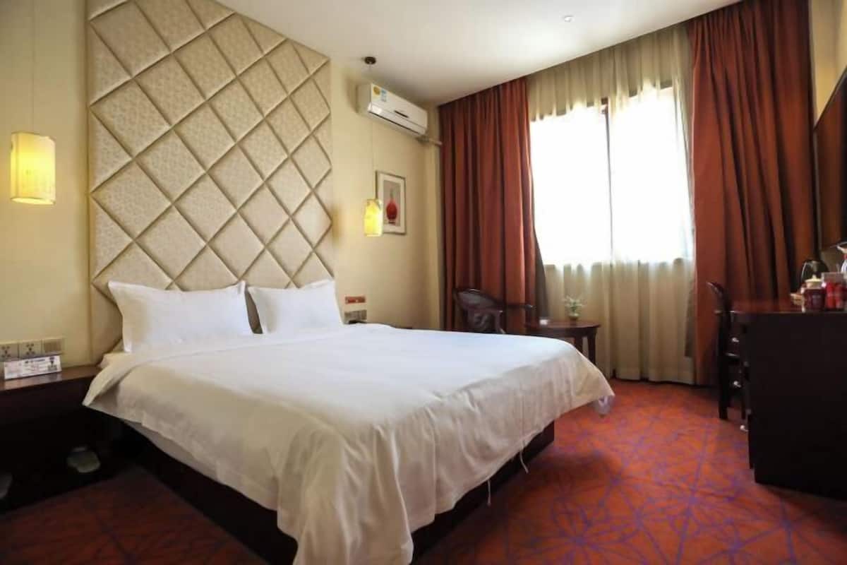 A hotel room with a large bed, a desk, a chair, and a window with curtains.