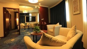 A hotel room with a sofa, a small table with a plant, a TV, and a dining area in the background. - The Tophams Hotel Suez (Wenzhou)
