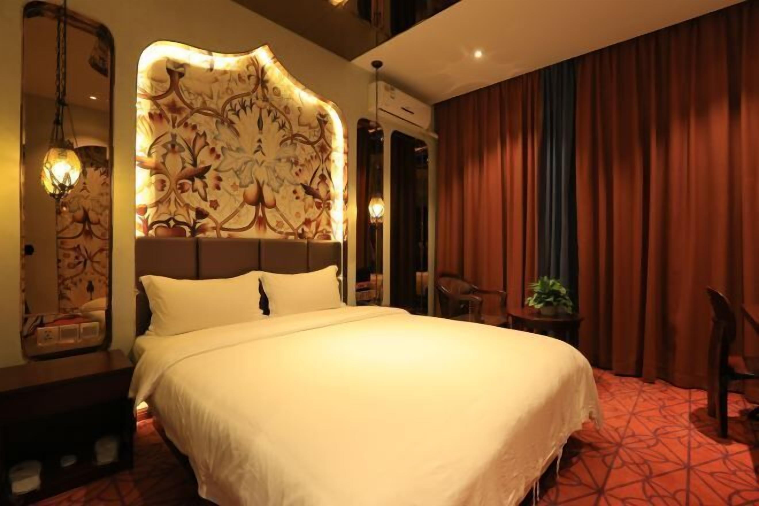 A hotel room with a large bed, a decorative headboard, a small table with a plant, and a chair.