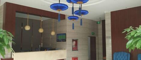 A reception area with a counter, blue chairs, hanging spherical lamps, and a large mirror.