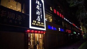 Un edificio con señalización iluminada en caracteres chinos, un número de teléfono visible y una fachada con puertas de cristal.