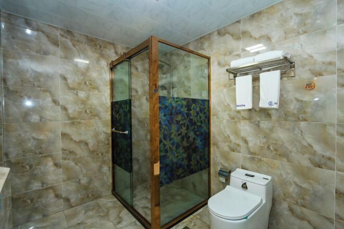 Un baño con ducha envuelta en vidrio, paredes de mármol, un inodoro y un perchero para toallas.