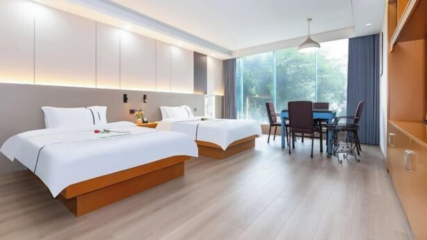 Una habitación de hotel moderna con dos camas, una mesa de comedor con sillas y ventanas amplias con vistas al exterior.