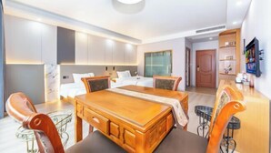 Habitación de hotel moderna con un gran comedor de madera, una zona de comedor separada, una cama con ropa blanca y armarios empotrados.