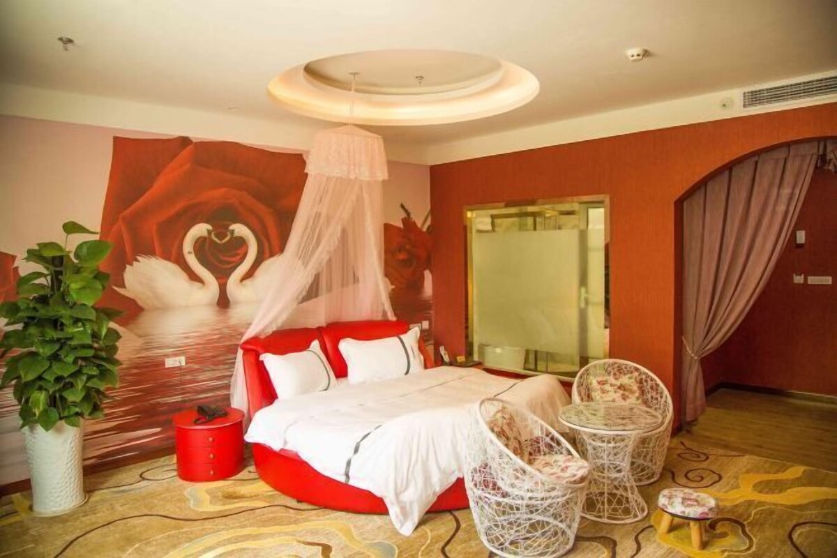 Habitación de hotel con una cama, una pared de acento roja, un espejo grande, una planta en maceta y un adorno de pared decorativo.