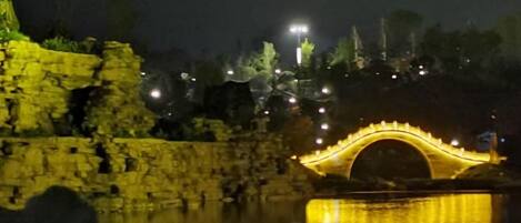 A stone bridge with a reflective surface, illuminated by lights, and a body of water in the foreground.
