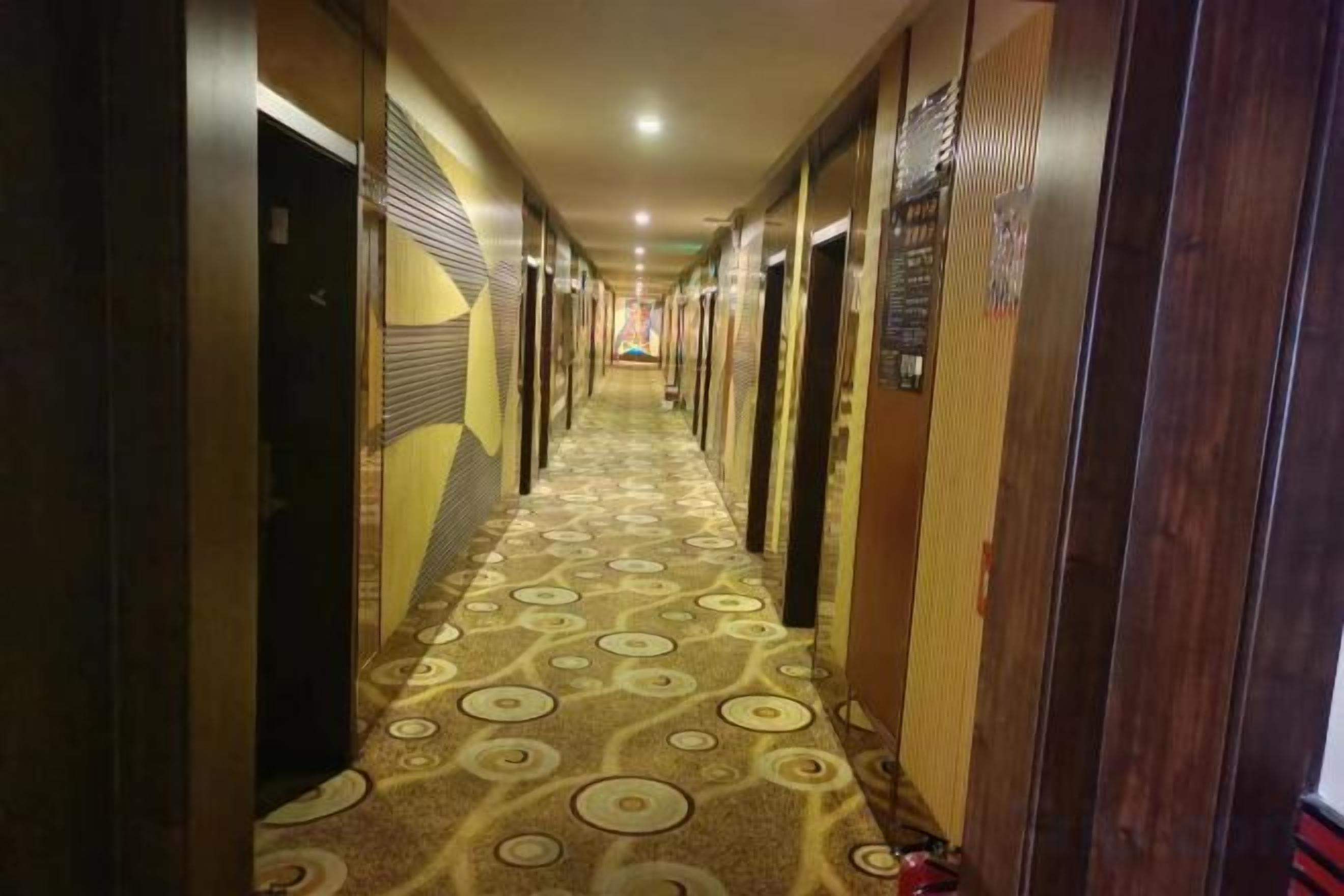 A hotel hallway with patterned carpet, doors on both sides, and a sign on the wall.