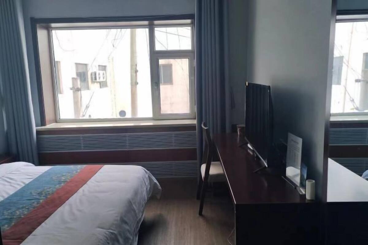 Ein Hotelzimmer mit Bett, Schreibtisch, Stuhl, einem Fenster mit Vorhängen und einem Heizkörper.