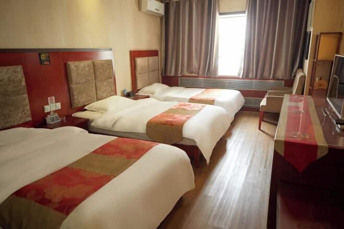 Ein Hotelzimmer mit zwei Betten, einem Schreibtisch, einem Fernseher und einem Fenster mit Vorhängen.
