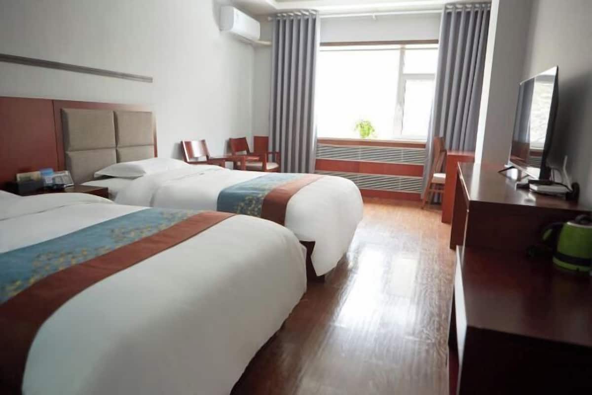 Ein Hotelzimmer mit zwei Betten, einem Schreibtisch, einem Stuhl, einem Fernseher und einem Fenster mit Vorhängen.